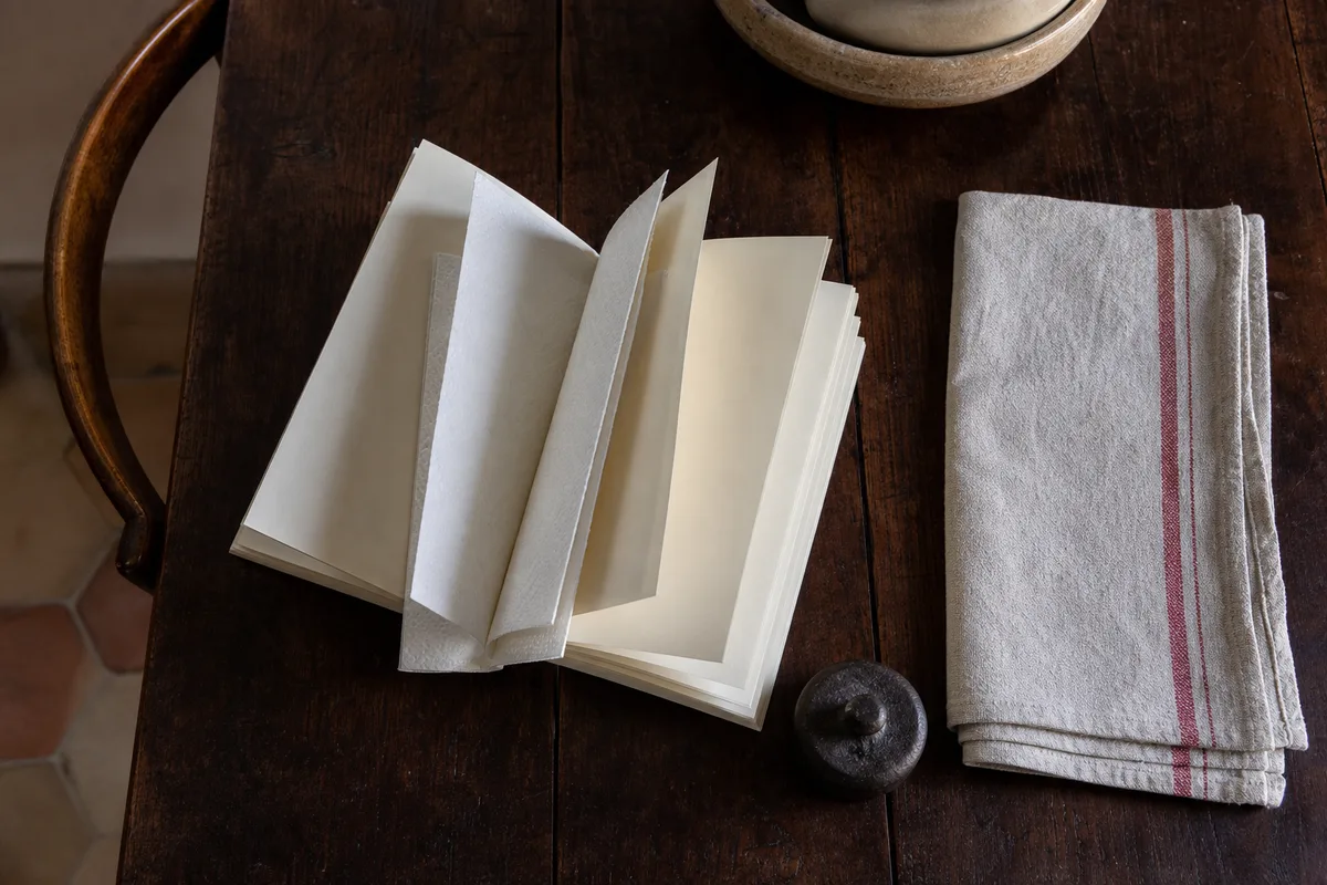Livre ouvert en éventail posé sur une table en bois, feuilles de papier absorbant intercalées entre les pages